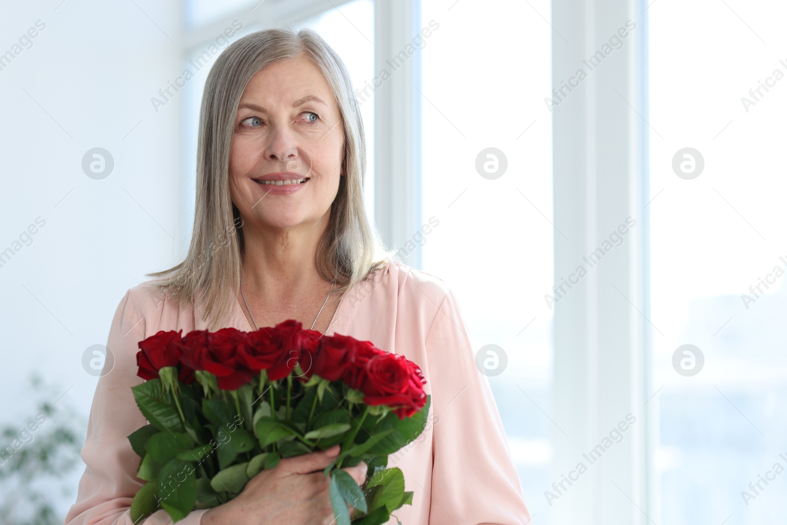 Photo of Smiling woman with bouquet of roses at home. Space for text