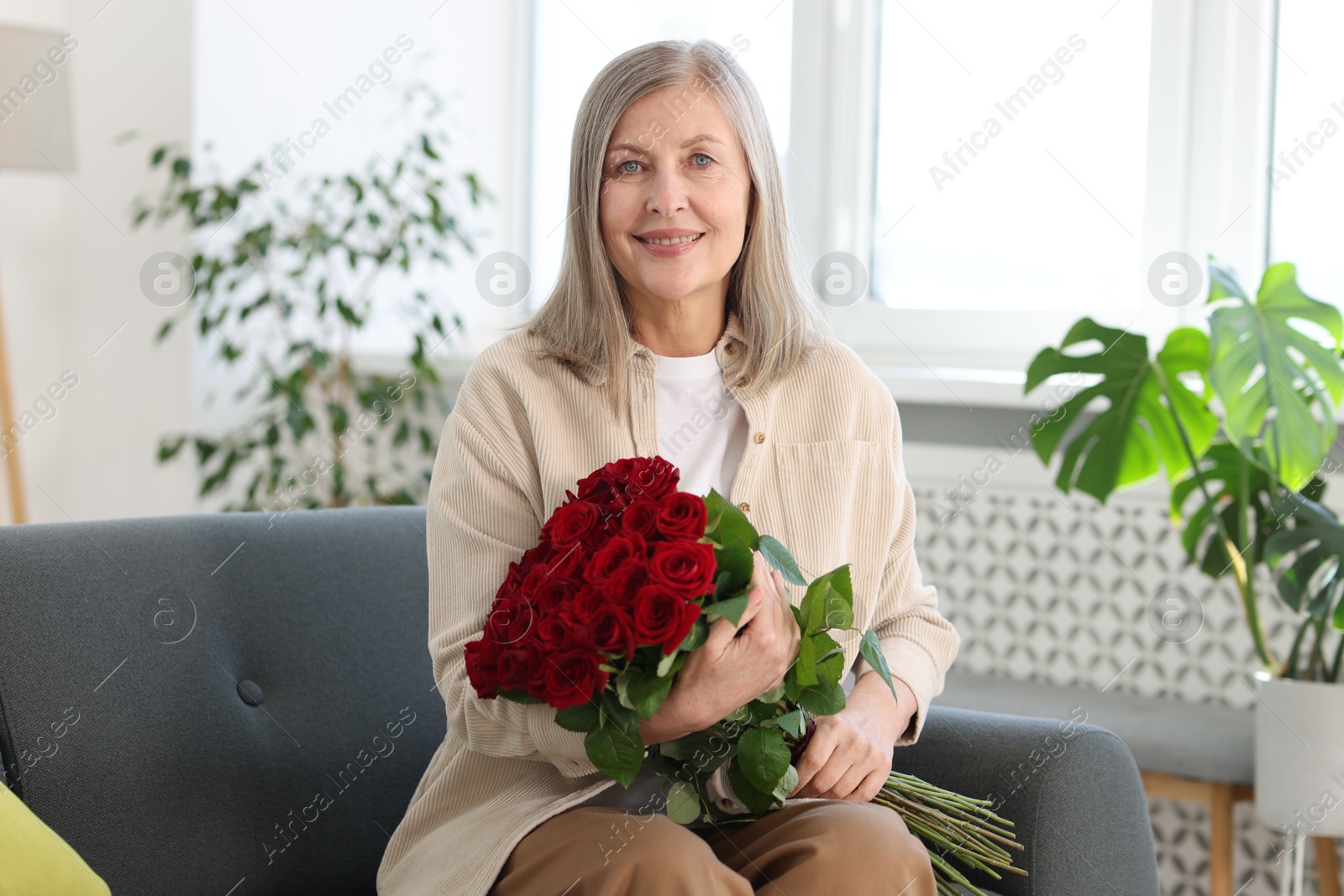 Photo of Smiling woman with bouquet of roses on sofa at home