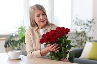 Photo of Beautiful woman with bouquet of roses at table indoors