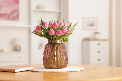 Photo of Bouquet of beautiful tulips in vase and book on table indoors, closeup