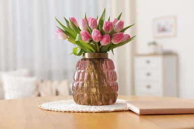 Photo of Bouquet of beautiful tulips in vase and book on table indoors, closeup