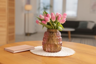 Photo of Bouquet of beautiful tulips in vase and book on table indoors, closeup