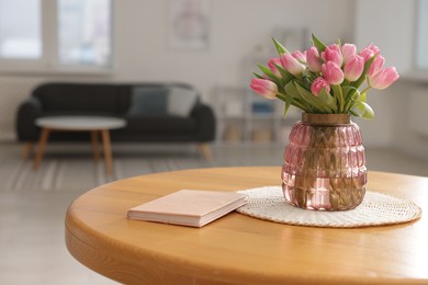 Photo of Bouquet of beautiful tulips in vase and book on table indoors