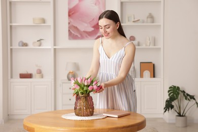 Photo of Smiling woman with bouquet of pink tulips at table indoors