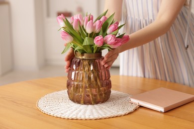 Photo of Woman with bouquet of pink tulips at wooden table indoors, closeup