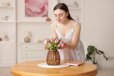 Photo of Woman with bouquet of pink tulips at table indoors