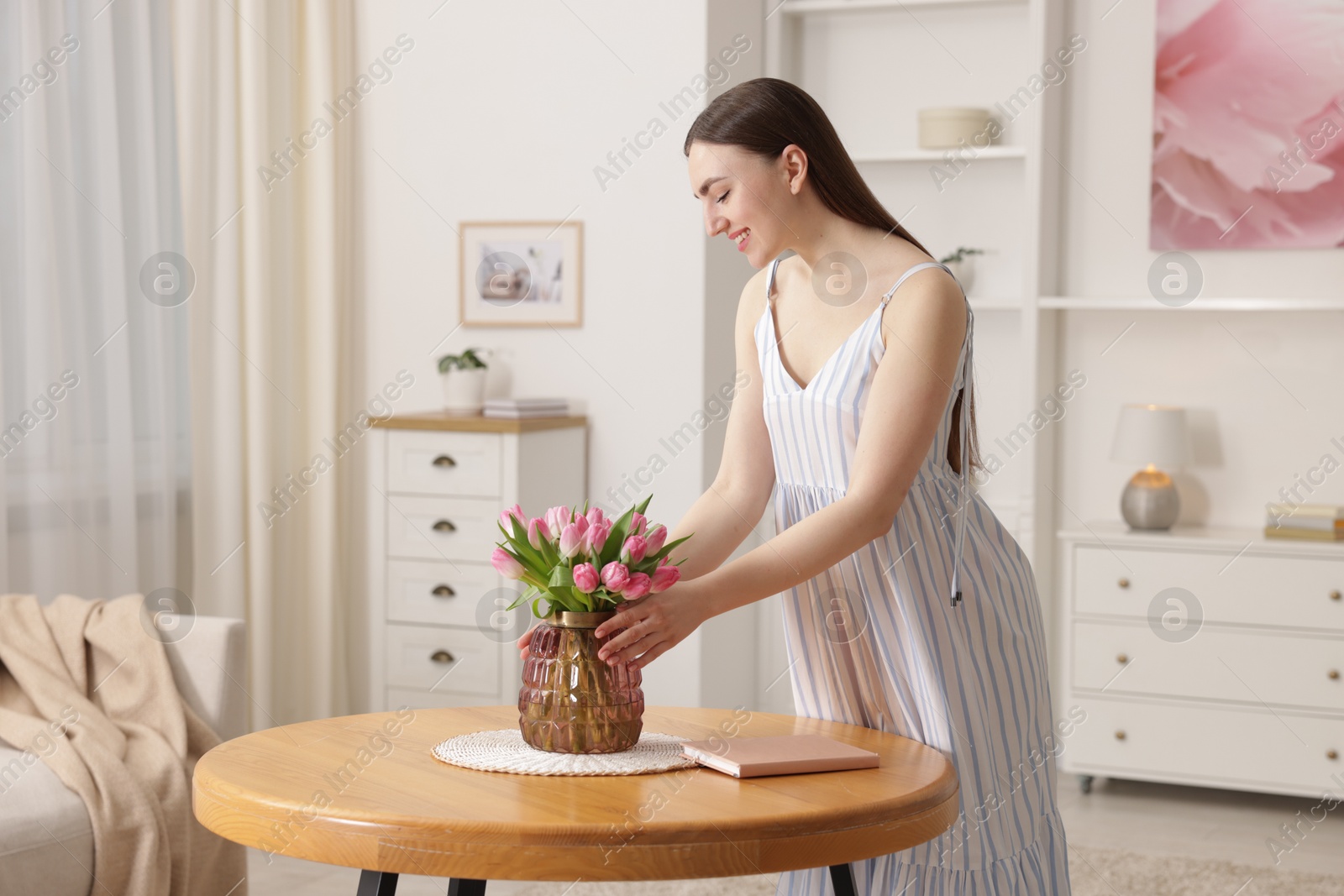 Photo of Smiling woman with bouquet of pink tulips at table indoors