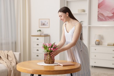 Smiling woman with bouquet of pink tulips at table indoors