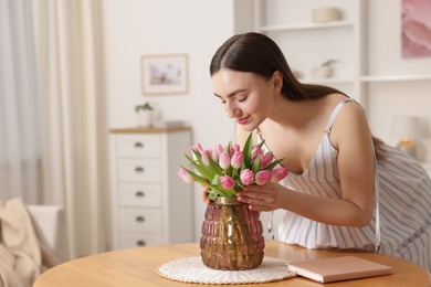 Woman with bouquet of pink tulips at table indoors. Space for text