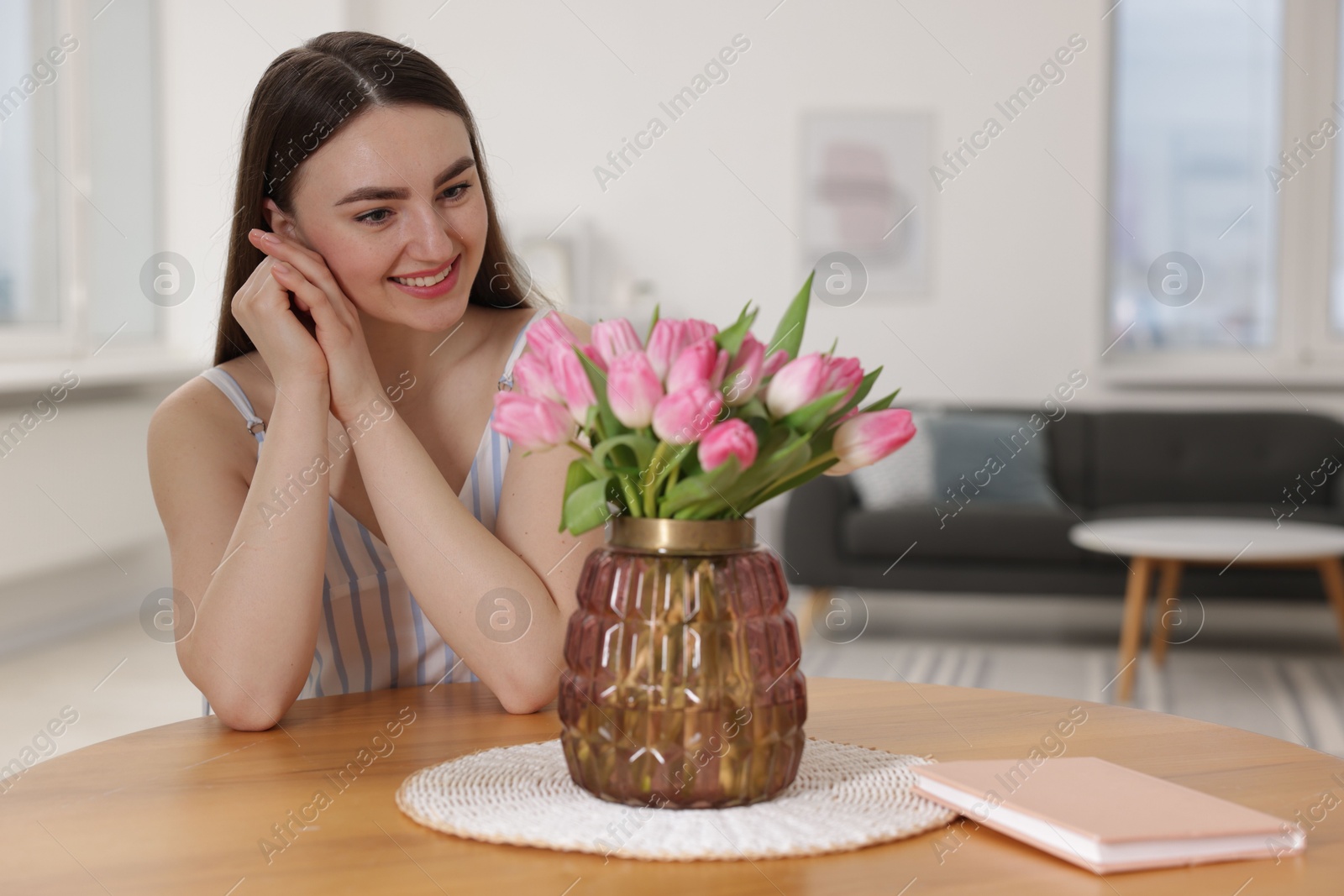 Photo of Smiling woman with bouquet of pink tulips at table indoors