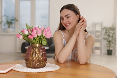 Photo of Smiling woman with bouquet of pink tulips at table indoors