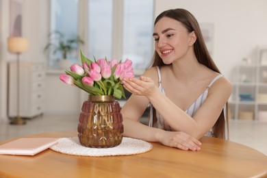 Photo of Smiling woman with bouquet of pink tulips at table indoors