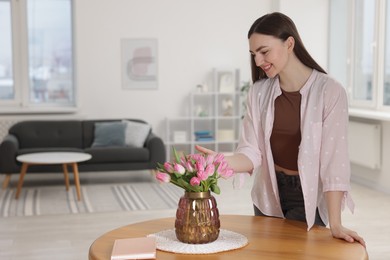 Smiling woman with bouquet of pink tulips at table indoors. Space for text