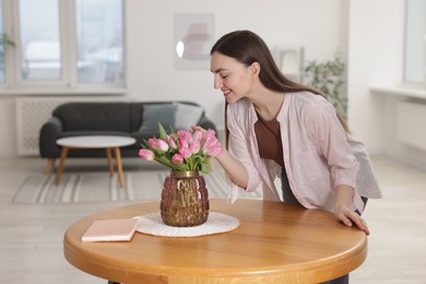 Smiling woman with bouquet of pink tulips at table indoors