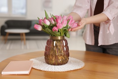 Photo of Woman with bouquet of pink tulips at wooden table indoors, closeup