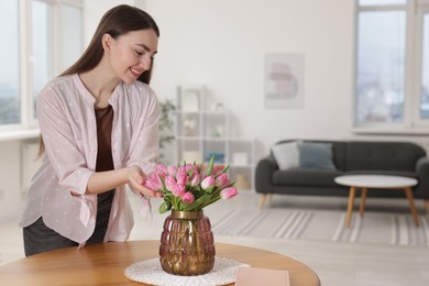 Photo of Smiling woman with bouquet of pink tulips at table indoors. Space for text