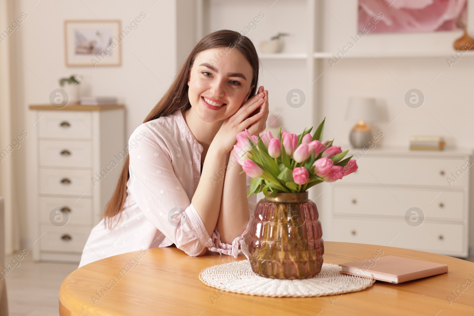 Photo of Smiling woman with bouquet of pink tulips at table indoors