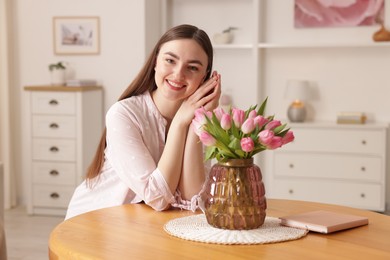 Photo of Smiling woman with bouquet of pink tulips at table indoors