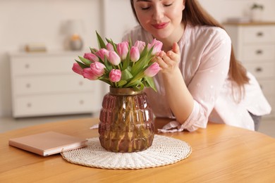 Woman with bouquet of pink tulips at wooden table indoors