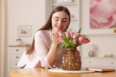 Photo of Smiling woman with bouquet of pink tulips at table indoors