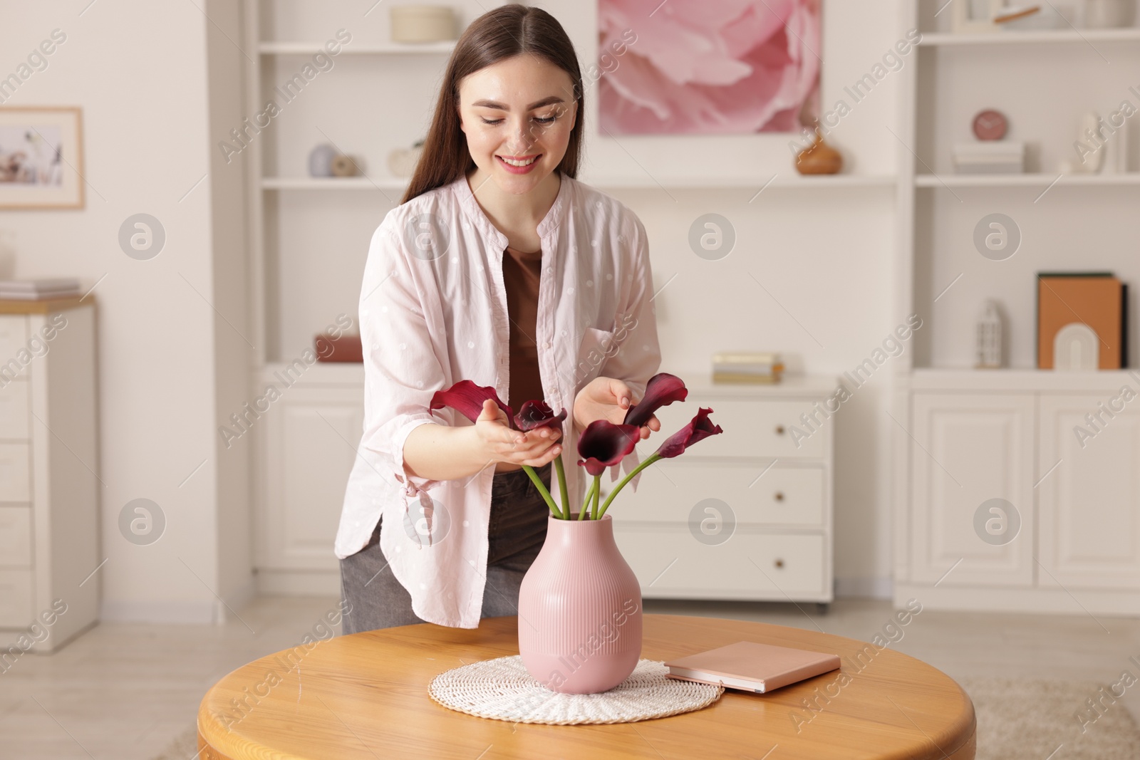 Photo of Smiling woman with bouquet of calla lily flowers at table indoors