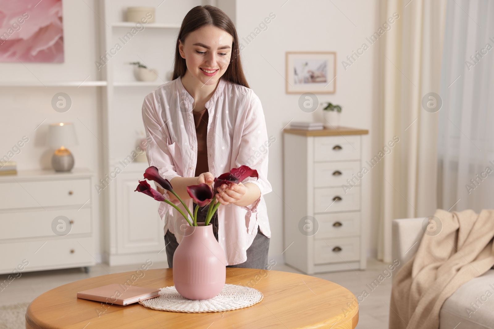 Photo of Smiling woman with bouquet of calla lily flowers at table indoors