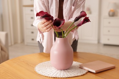 Photo of Woman with bouquet of calla lily flowers at table indoors, closeup