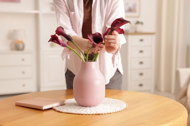 Photo of Woman with bouquet of calla lily flowers at table indoors, closeup