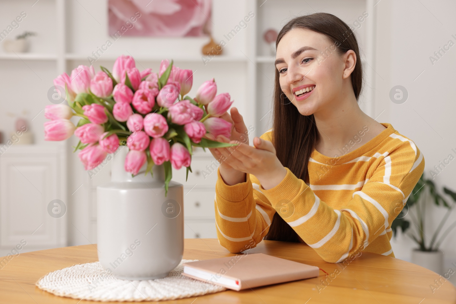 Photo of Smiling woman with bouquet of pink tulips at table indoors