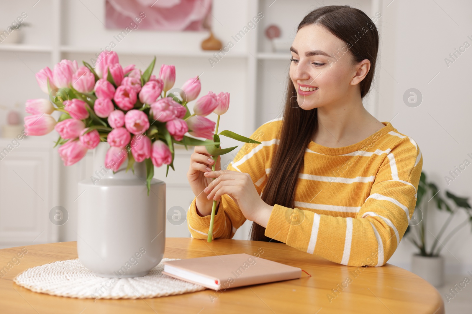 Photo of Smiling woman with bouquet of pink tulips at table indoors