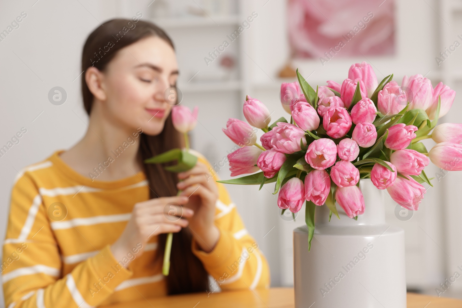 Photo of Woman sniffing tulip at table indoors, focus on bouquet