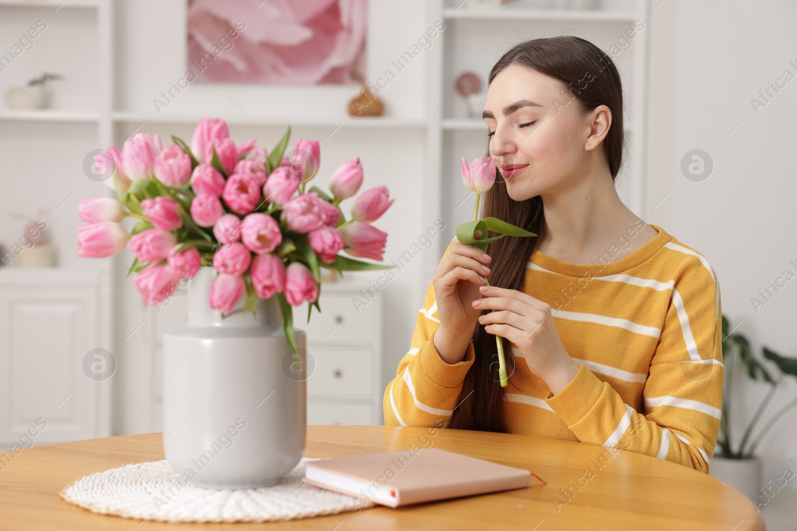 Photo of Woman sniffing tulip at table with bouquet indoors, selective focus