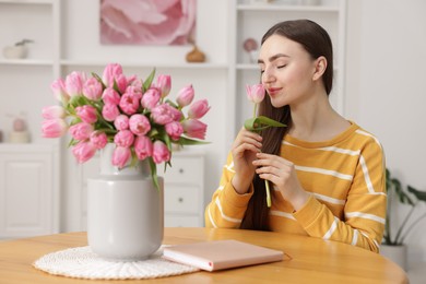 Woman sniffing tulip at table with bouquet indoors, selective focus