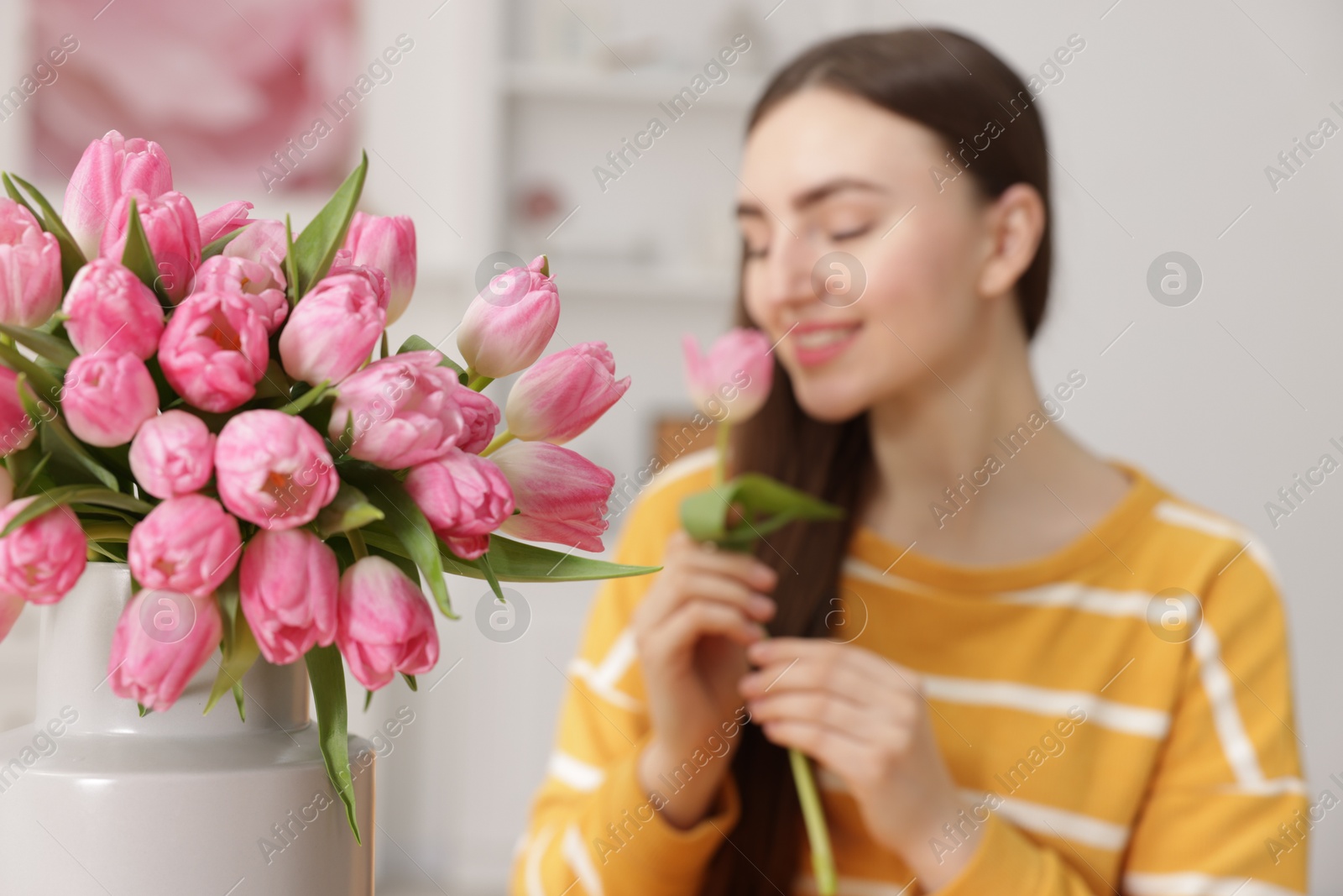 Photo of Woman sniffing tulip indoors, focus on bouquet