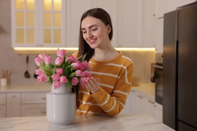 Smiling woman with bouquet of pink tulips at table in kitchen