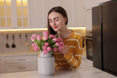 Woman with bouquet of pink tulips at table in kitchen