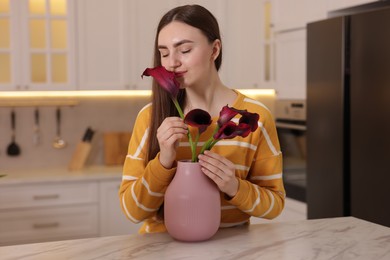 Woman with bouquet of calla lily flowers at table in kitchen