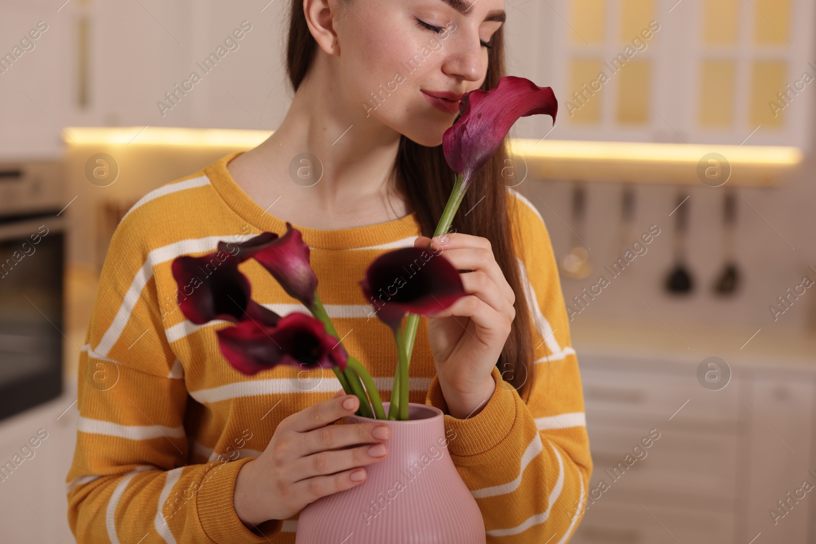 Photo of Woman sniffing calla lily flowers in kitchen