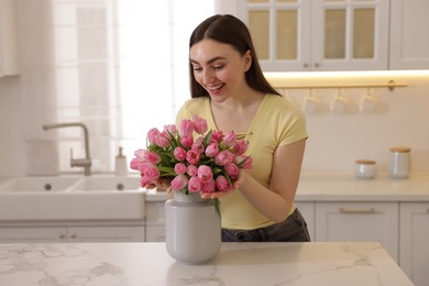 Photo of Happy woman with bouquet of pink tulips at table in kitchen