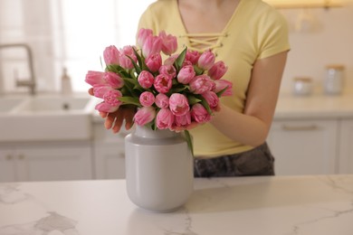 Photo of Woman with bouquet of pink tulips at table in kitchen, closeup