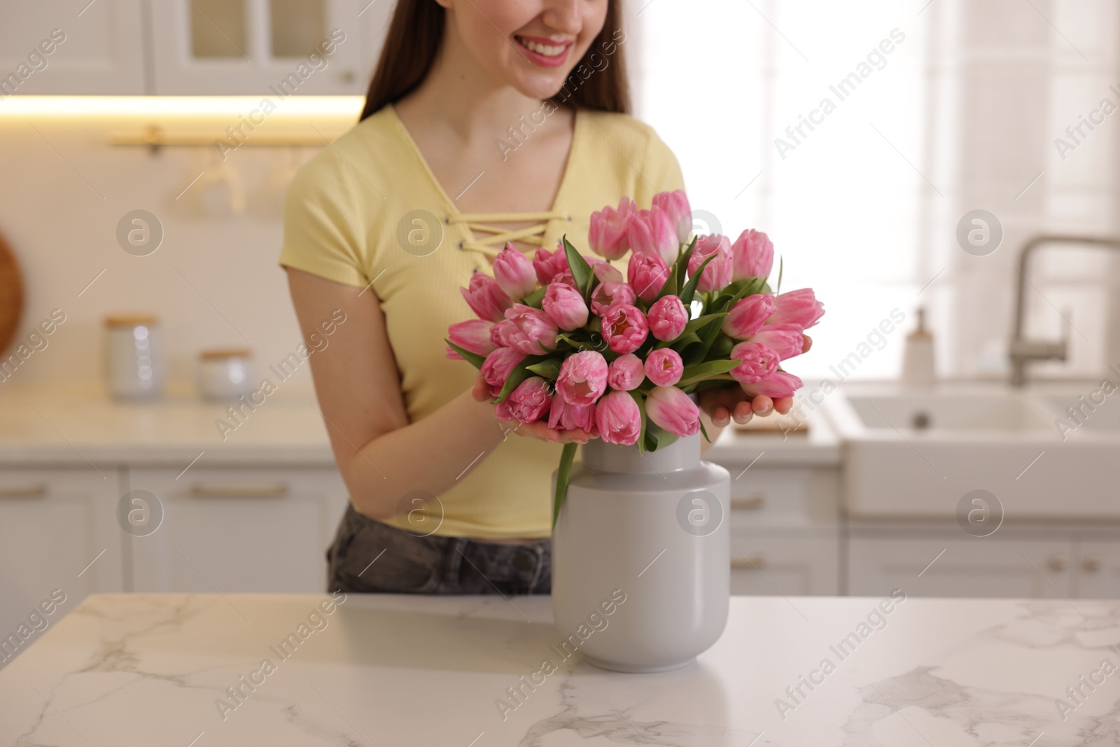 Photo of Smiling woman with bouquet of pink tulips at table in kitchen, closeup