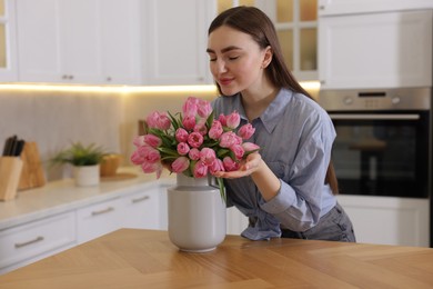 Woman sniffing bouquet of pink tulips at table in kitchen