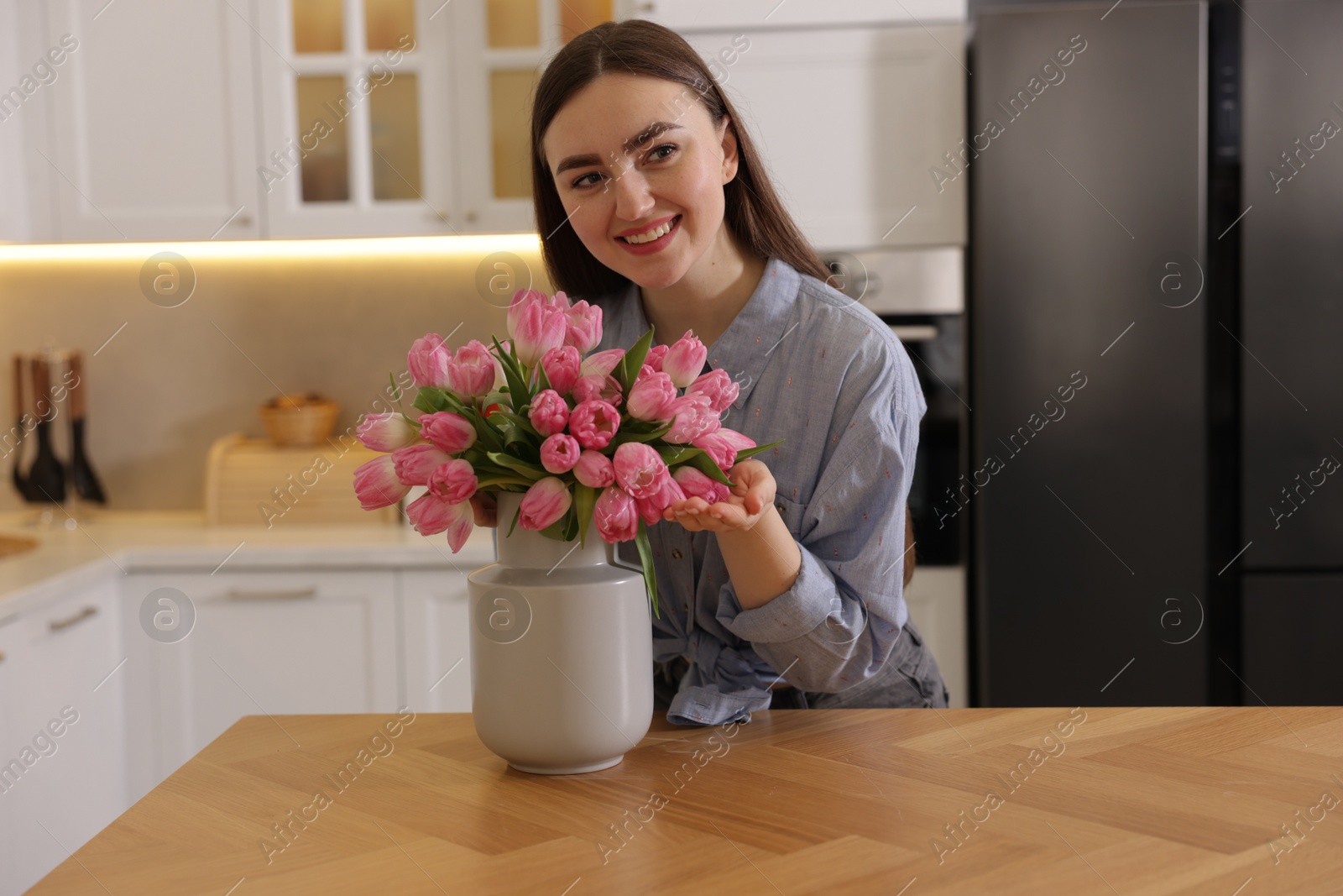 Photo of Smiling woman with bouquet of pink tulips at table in kitchen