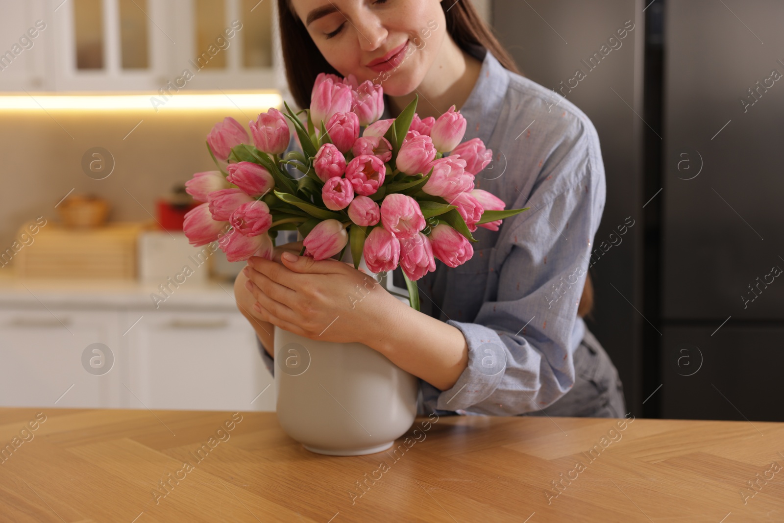 Photo of Woman with bouquet of pink tulips at wooden table in kitchen, closeup