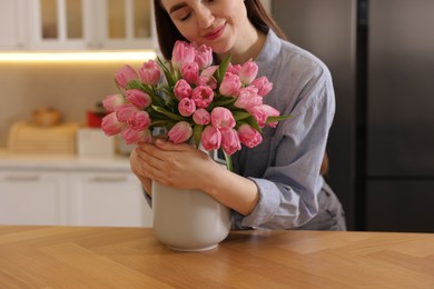 Woman with bouquet of pink tulips at wooden table in kitchen, closeup