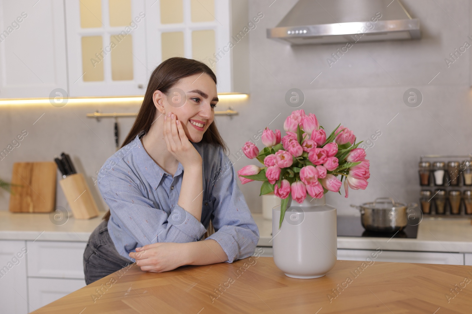 Photo of Smiling woman with bouquet of pink tulips at table in kitchen