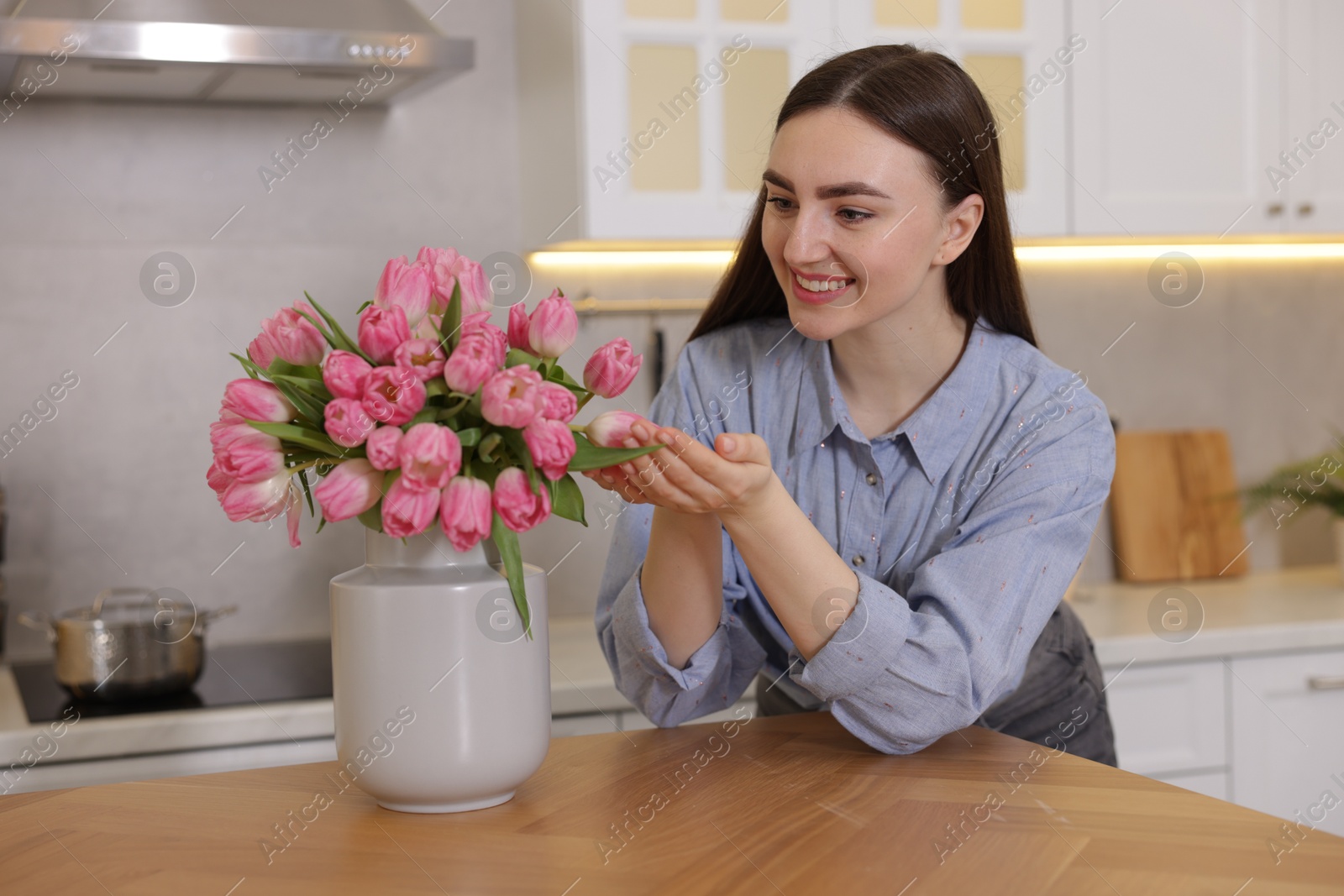 Photo of Smiling woman with bouquet of pink tulips at table in kitchen