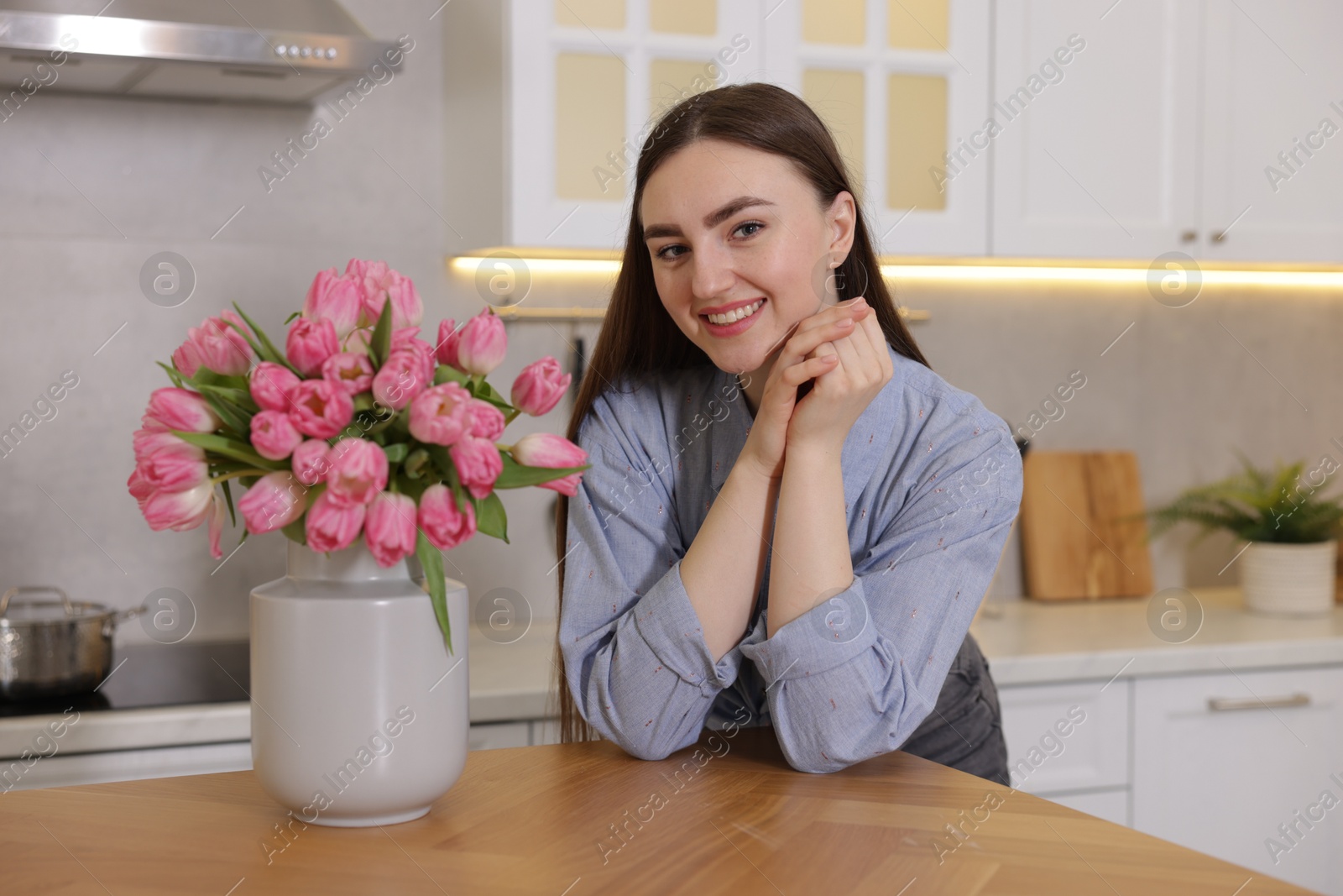 Photo of Smiling woman with bouquet of pink tulips at table in kitchen