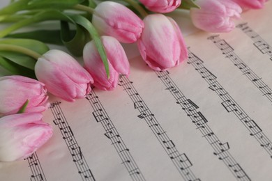 Photo of Beautiful tulips on sheet with music notes, closeup