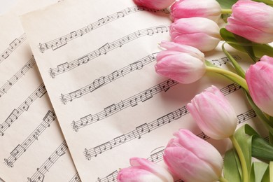 Photo of Beautiful tulips on sheets with music notes, top view